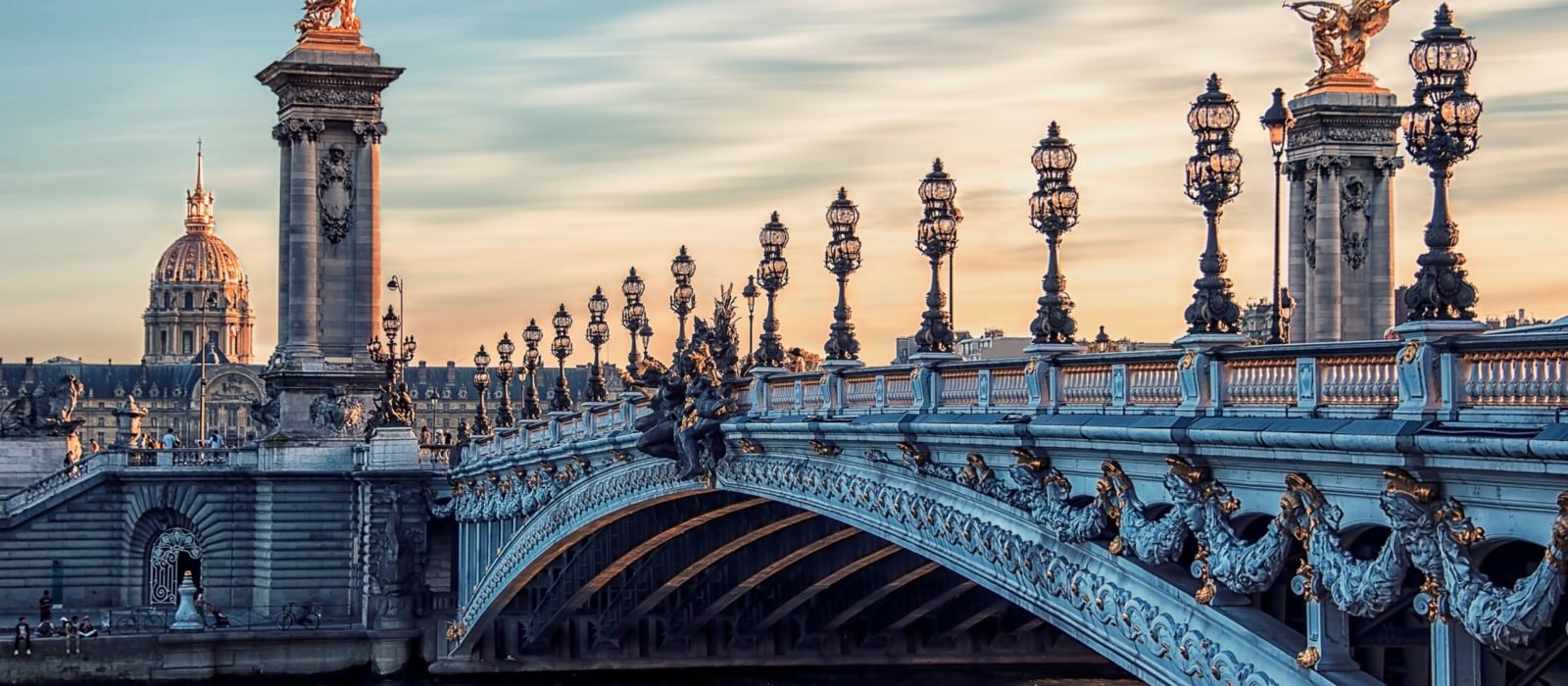 Alexandre III bridge in Paris, a grand and ornate arched bridge over the River Seine with gothic black lampposts, and gold detailed statues on plinths